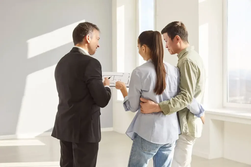 In an empty room, a man and woman stand side by side, observing the space with thoughtful expressions.