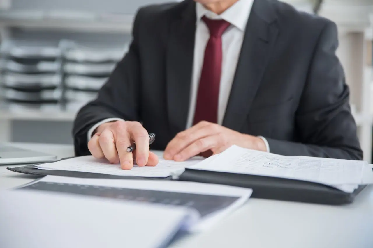 A man in a suit is writing on a piece of paper at a desk, focused on his task.