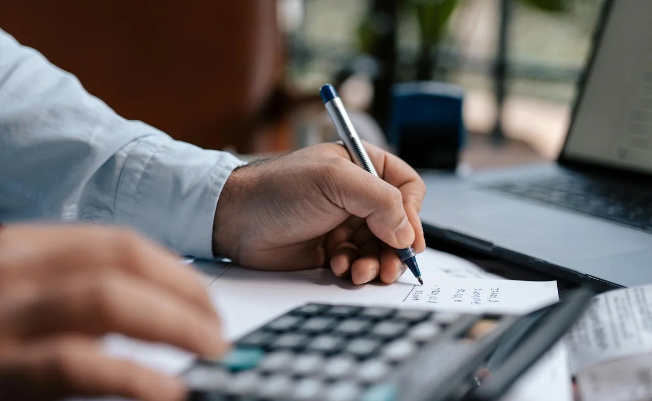 Man writing on paper while using a calculator, focused on calculations and notes.