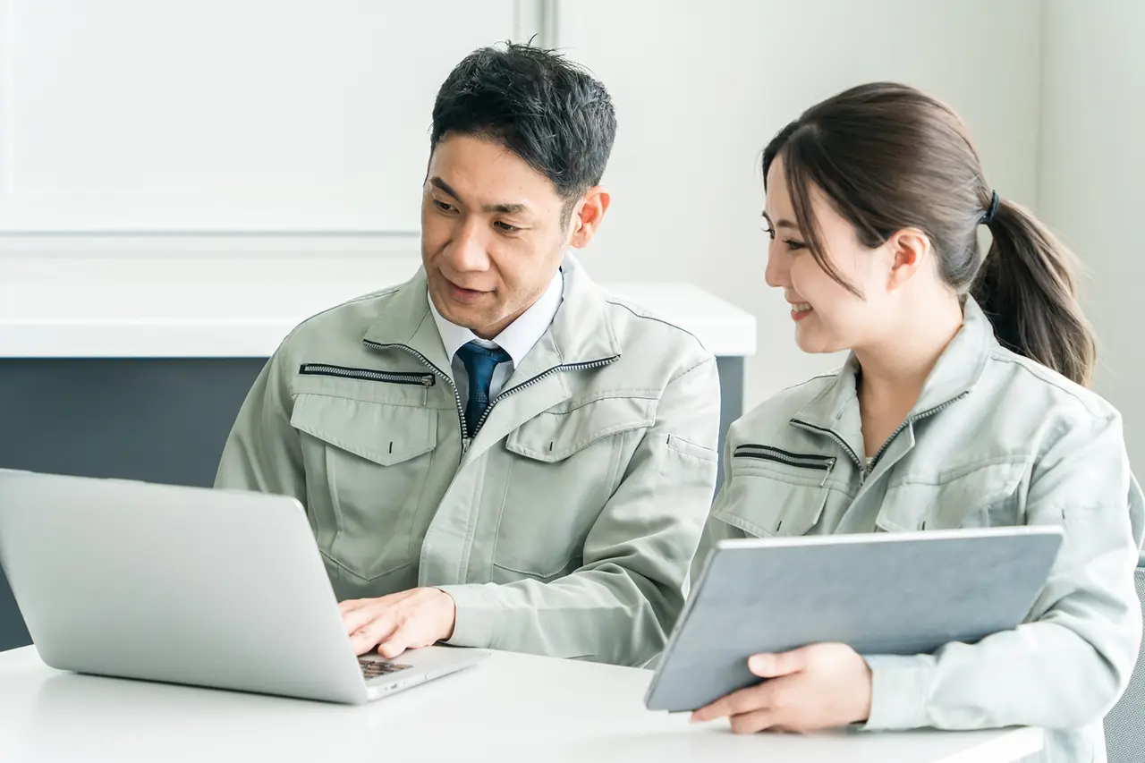 Asian man and woman in business suits collaborating while looking at a laptop screen.