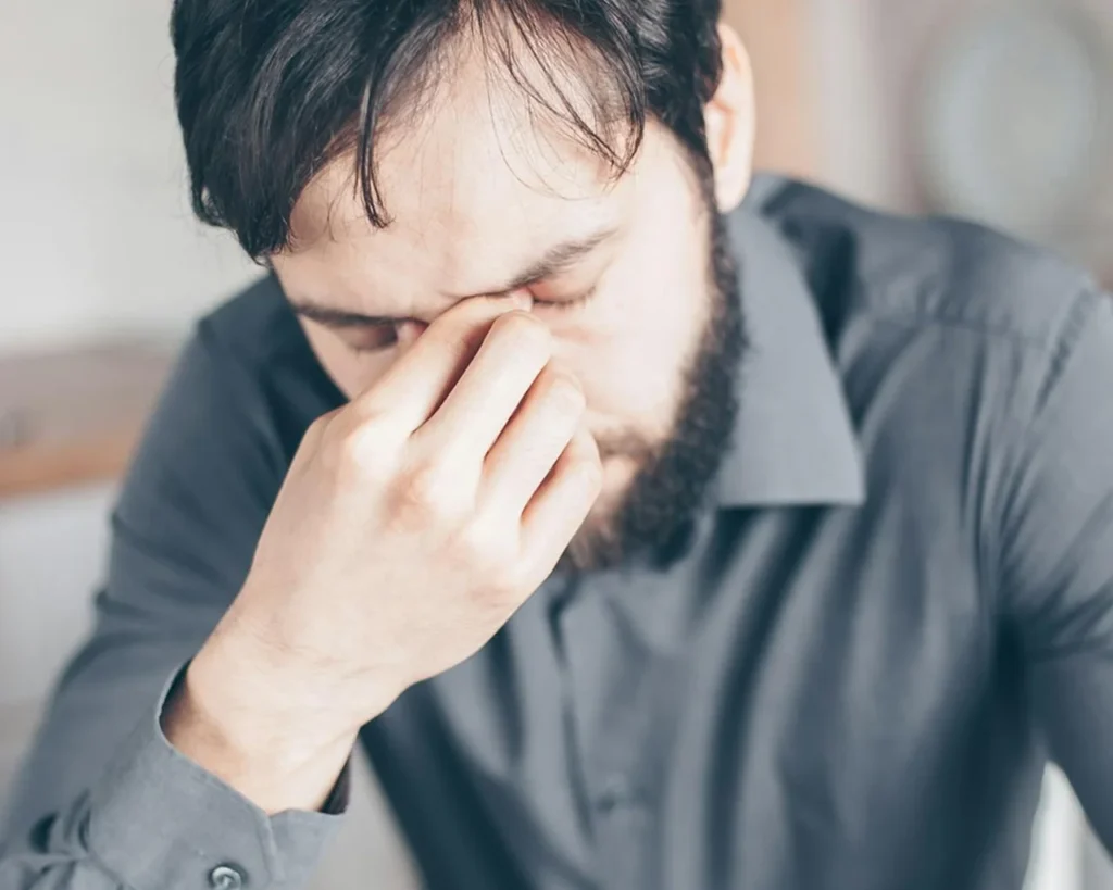 A bearded man covers his eyes with his hand, expressing a moment of contemplation or surprise.
